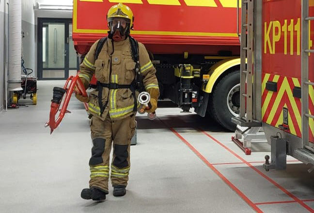 Täysissä varusteissa oleva palomies kävelee tuotteen ja jatkoputken kanssa.