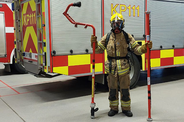 Palomies täydellisessä varustuksessa pitää kädessään tuotetta ja jatkoputkea.